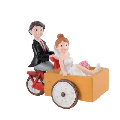 Figurine en résine, couple de mariés installés sur un triporteur rouge.