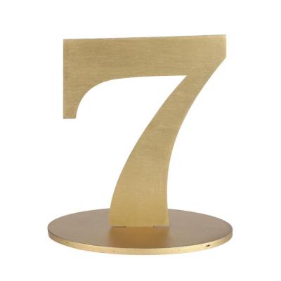 En bois coloris or, le chiffre 7 posé sur son  support à utiliser comme marque table ou en déco de table anniversaire.