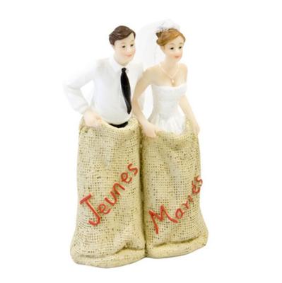 Une figurine en résine de 13 cm représentant un couple de mariés dans un sac de jute sur lequel est inscrit Jeunes mariés.