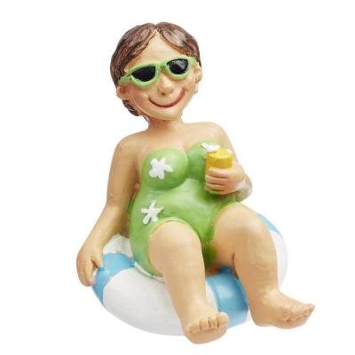 Une petite figurine de femme représentée en maillot de bain et assise sur une bouée, indispensable pour vos décorations de table de fêtes thème mer, vacances et soleil