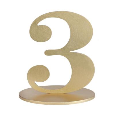 En bois coloris or, le chiffre 3 posé sur son  support à utiliser comme marque table ou en déco de table anniversaire.